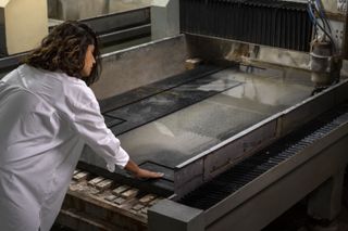 A young woman dressed in a white shirt works on some stone surfacing tiles in an industrial workshop.