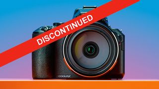 Front view of a Nikon Coolpix P950 camera with a red "DISCONTINUED" banner across it, on an orange surface with a gradient background.