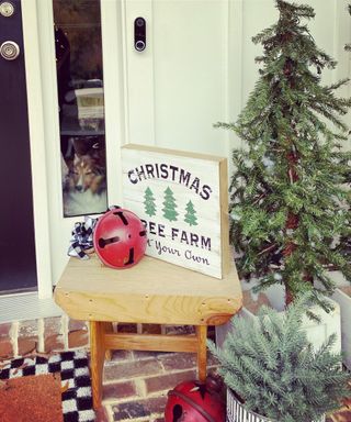 Christmas porch decor with festive signage jingle bells tree and dog in window