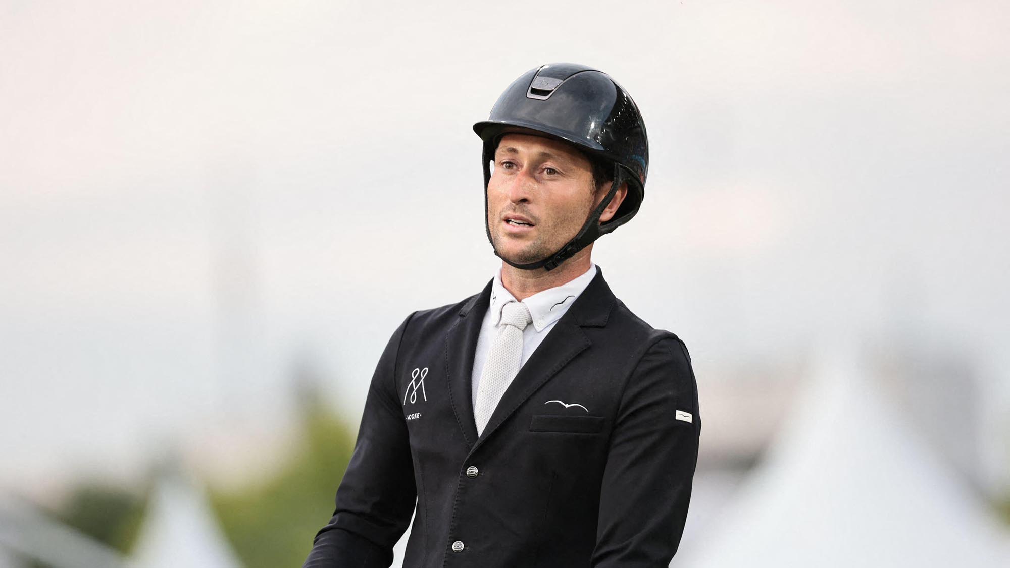 British showjumper Adrian Whiteway wearing a black show jacket and riding hat with a white shirt and tie.