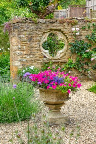 flowers flooding from a stone planter in front of a cotswold stone wall