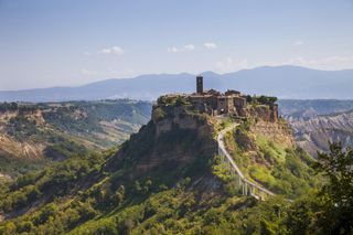 A hilltop village immersed in vegetation is captured from afar at golden hour.