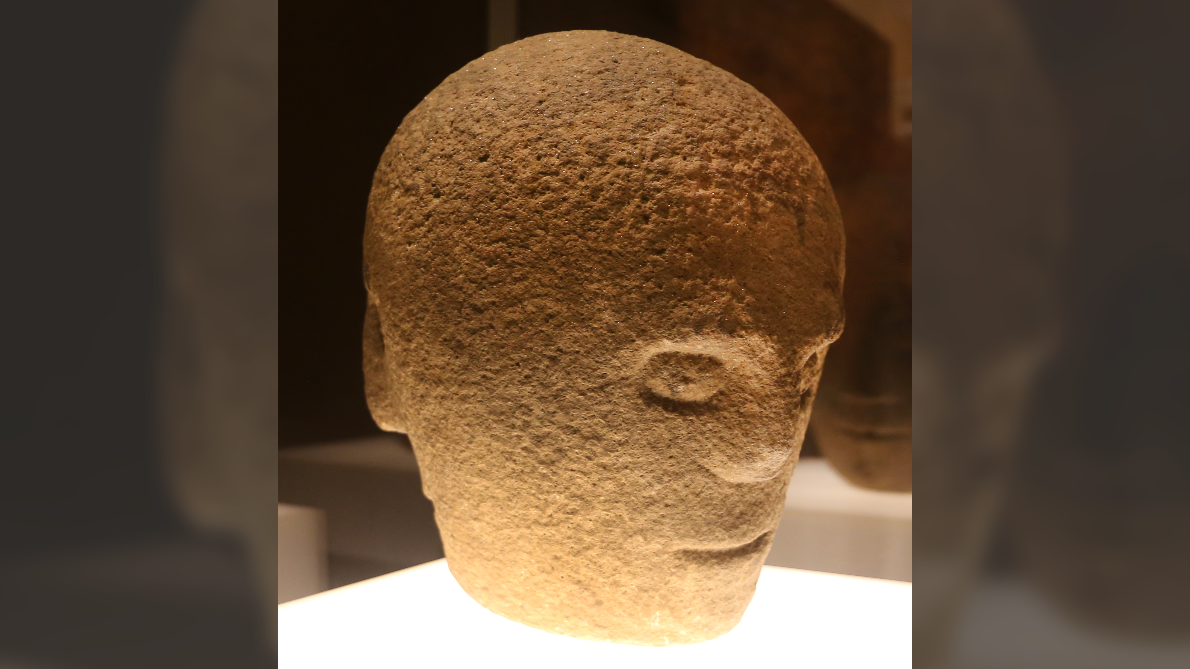 a sandstone head carved with multiple features is lit from below and appears spooky