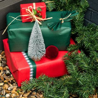 red and green wrapped christmas presents sitting on gravel, with a faux green leaf garland trailing behind them