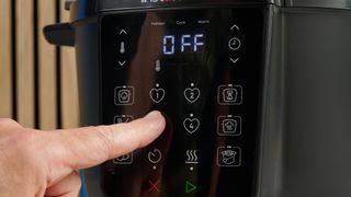 a black pressure cooker photographed against a blue background, showing its cooking presets, steam release valve, and Instant Pot branding