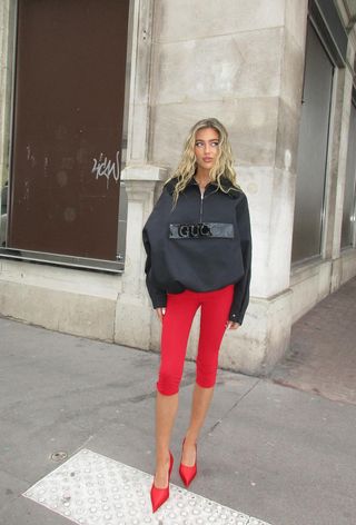 a photo photo showing what colors go with red, specifically a woman wearing a red capri pants with a black rain jacket and red pumps