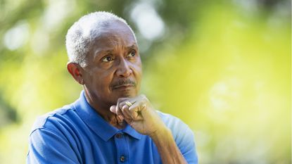 A retiree looks thoughtful as he stands outside.