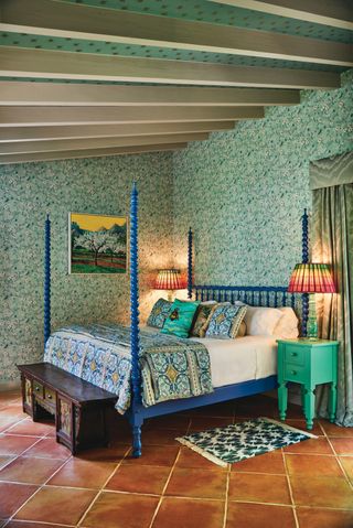 bedroom with green floral wallpaper, blue 4 poster bed and tiled floors