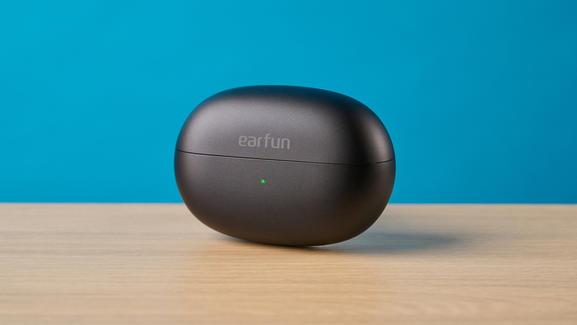EarFun Clip 2 in black on table photographed in front of a blue background