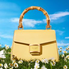Butter yellow Kate Spade handbag in on grass with blue sky behind it
