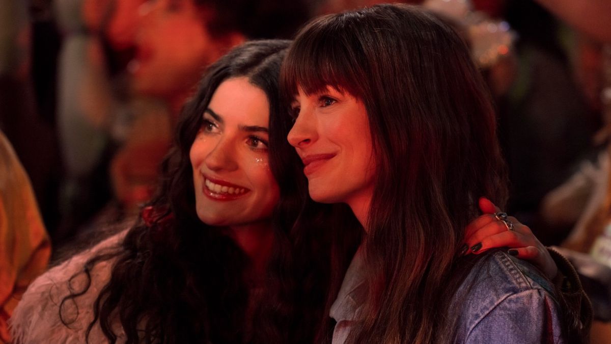 Anne Hathaway as &#039;Solène&#039; and Ella Rubin as &#039;Izzy&#039; smiling while standing right next to each other in the crowd of a concert.