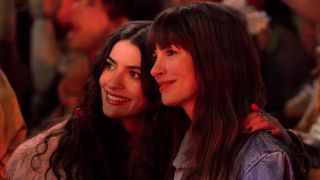 Anne Hathaway as 'Solène' and Ella Rubin as 'Izzy' smiling while standing right next to each other in the crowd of a concert.