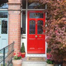 Victorian house, original red front door with stained glass windows, arched brickwork, porch, tiled path, potted plants, trees