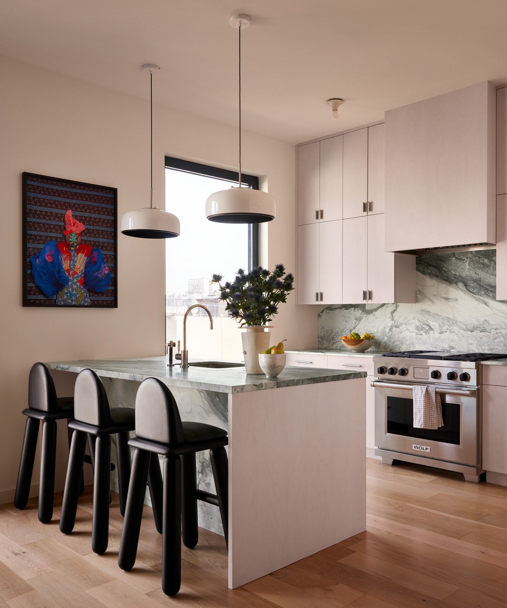 Kitchen with pink cabinets, marble island and backsplash, black bar stools and two pendant lights