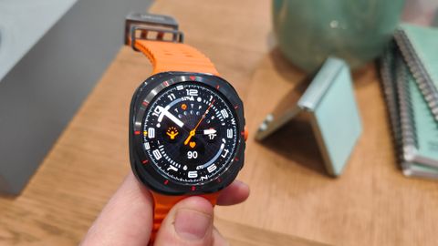 Samsung Galaxy Watch Ultra ihmisen kädessä puisen pöydän yläpuolella