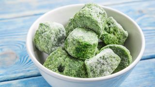 Blocks of frozen spinach in a bowl on a wooden table