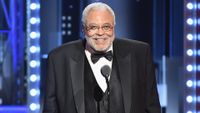 a man in a suit speaks into a microphone on a stage at an awards ceremony