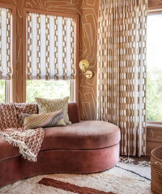 corner of snug living room with '80s terracotta color scheme, patterned terracotta wallpaper and curtains, curved pink sofa