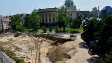 We see Victorian buildings in the background and a large dig site in the foreground.
