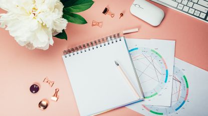 Open Notebook for writing ideas and astrological birth natal chart laying on pink background. Computer keyboard and mouse nearby. Idea of Astrological Consultation. Flat lay in girly style