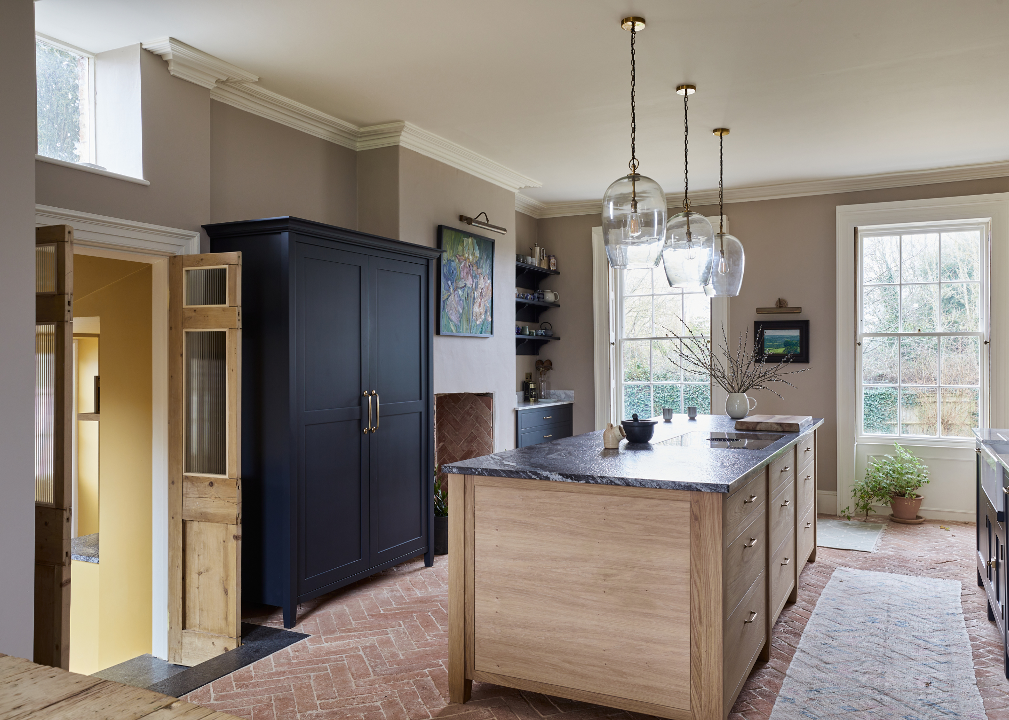 A modern traditional kitchen with herringbone brick floor tiles two small double doors open with steps down to a boot room/utility