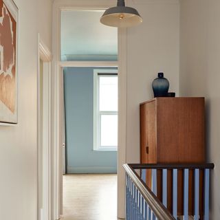 Hallway landing with white walls and blue painted stair rods and abstract artwork
