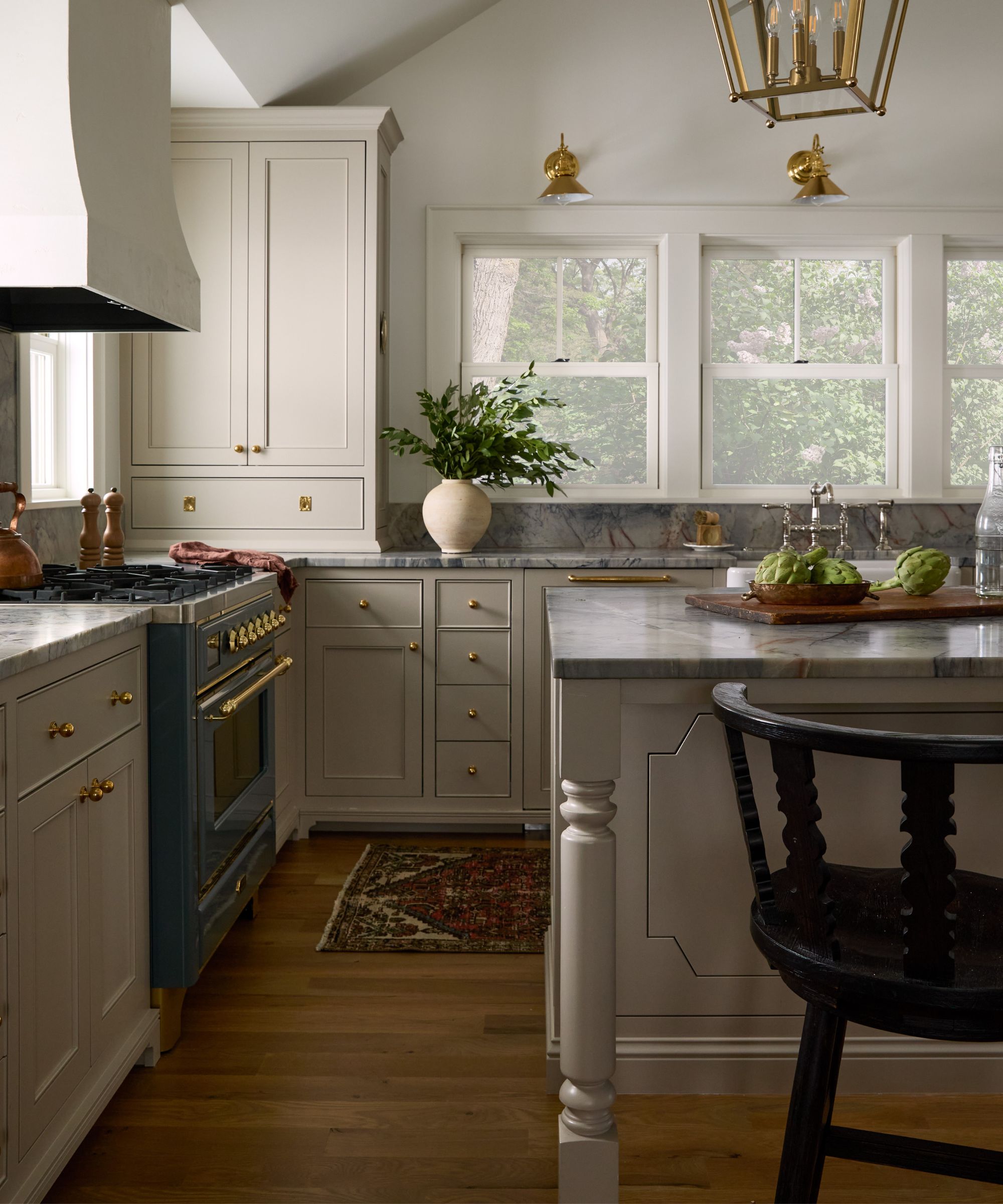 earthy neutral kitchen with large windows out to the lakeside view, a large plaster cooker hood, and blue marble countertops