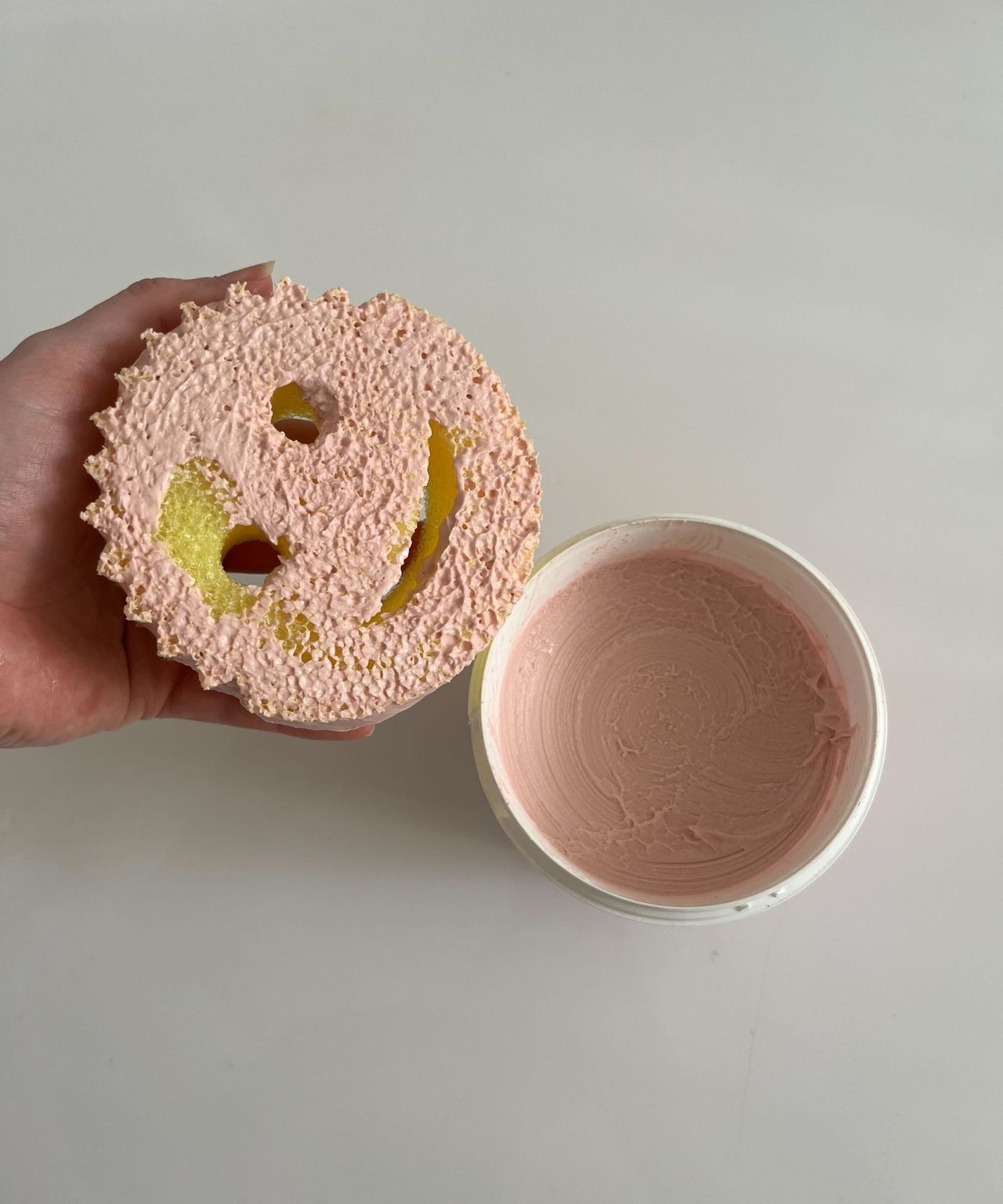A yellow Scrub Daddy sponge covered in The Pink Stuff paste, next to a tub of the paste