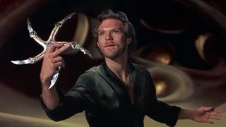 Still from the science fantasy movie Krull (1983). A man is holding a weapon in his right hand. It is a glaive – a 5-pointed star-shaped weapon with curved blades at each point.