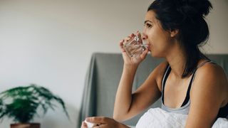 A woman sits in bed drinking a glass of water.