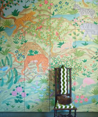 Colorful green and pink wallpaper, jungle inspired scene with animals, tall wooden chair placed in front of wall with white and green striped upholstery