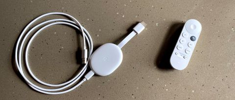 The chromecast with google tv streaming device pictured next to its white remote on a grey surface