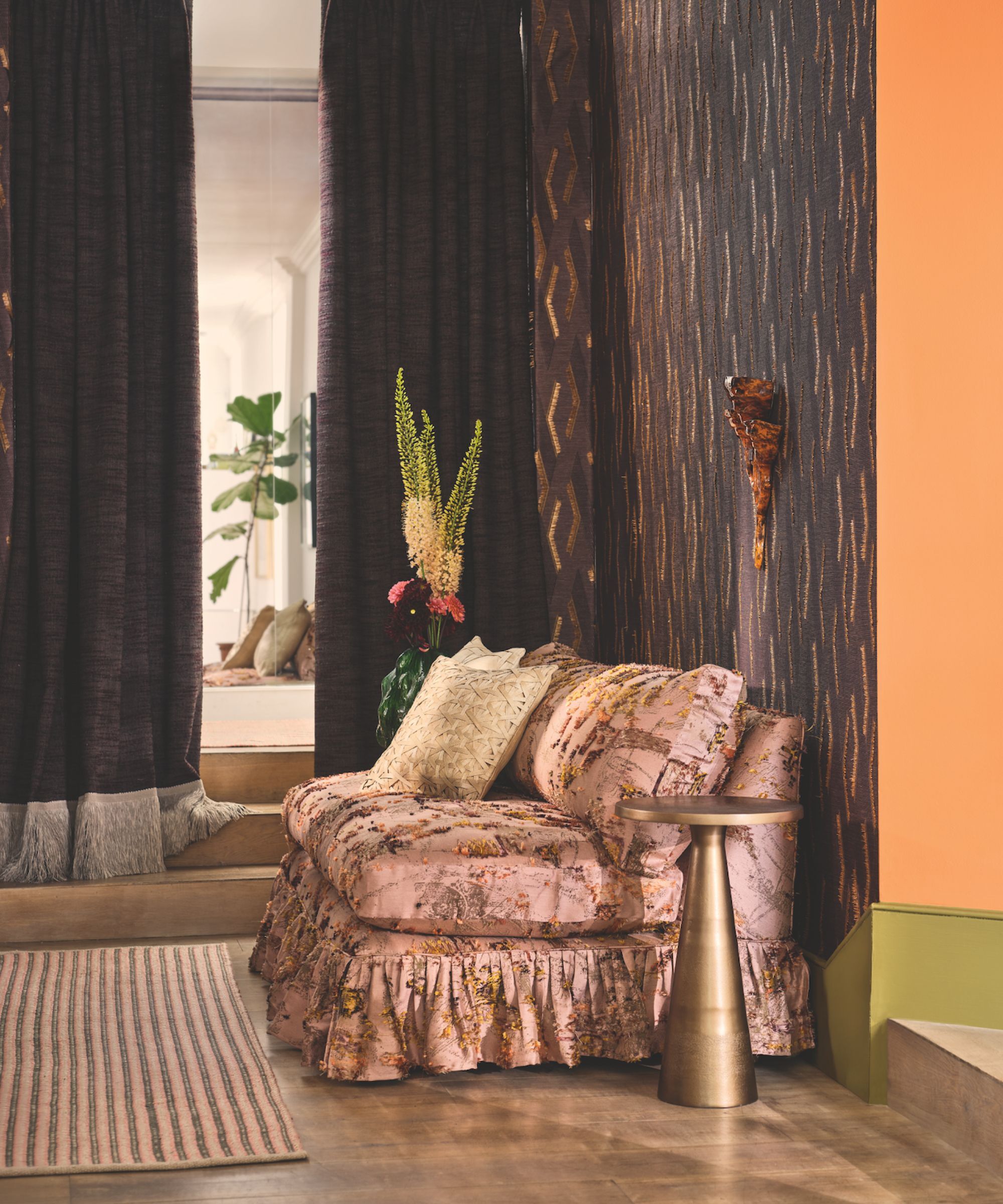 A textured wallcovering and pink satin fringed sofa