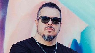 Iggor Cavalera wearing sunglasses and standing against a multi coloured wall