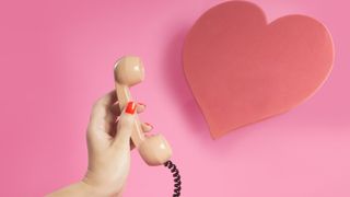 woman holding pink phone beside red paper heart on pink background