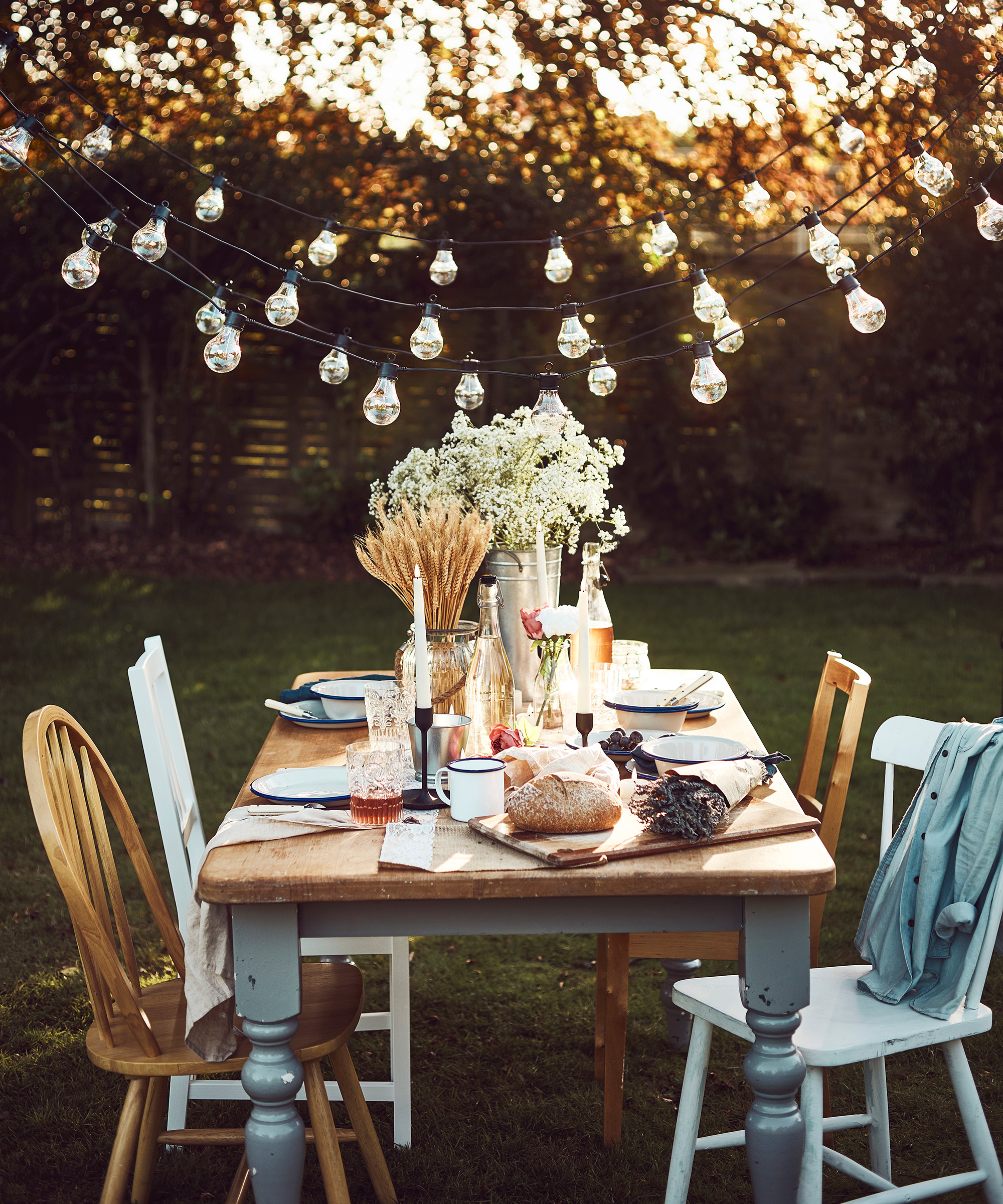 Garden decorating ideas showing a wooden table and chairs with a spread of food laid out underneath string lights