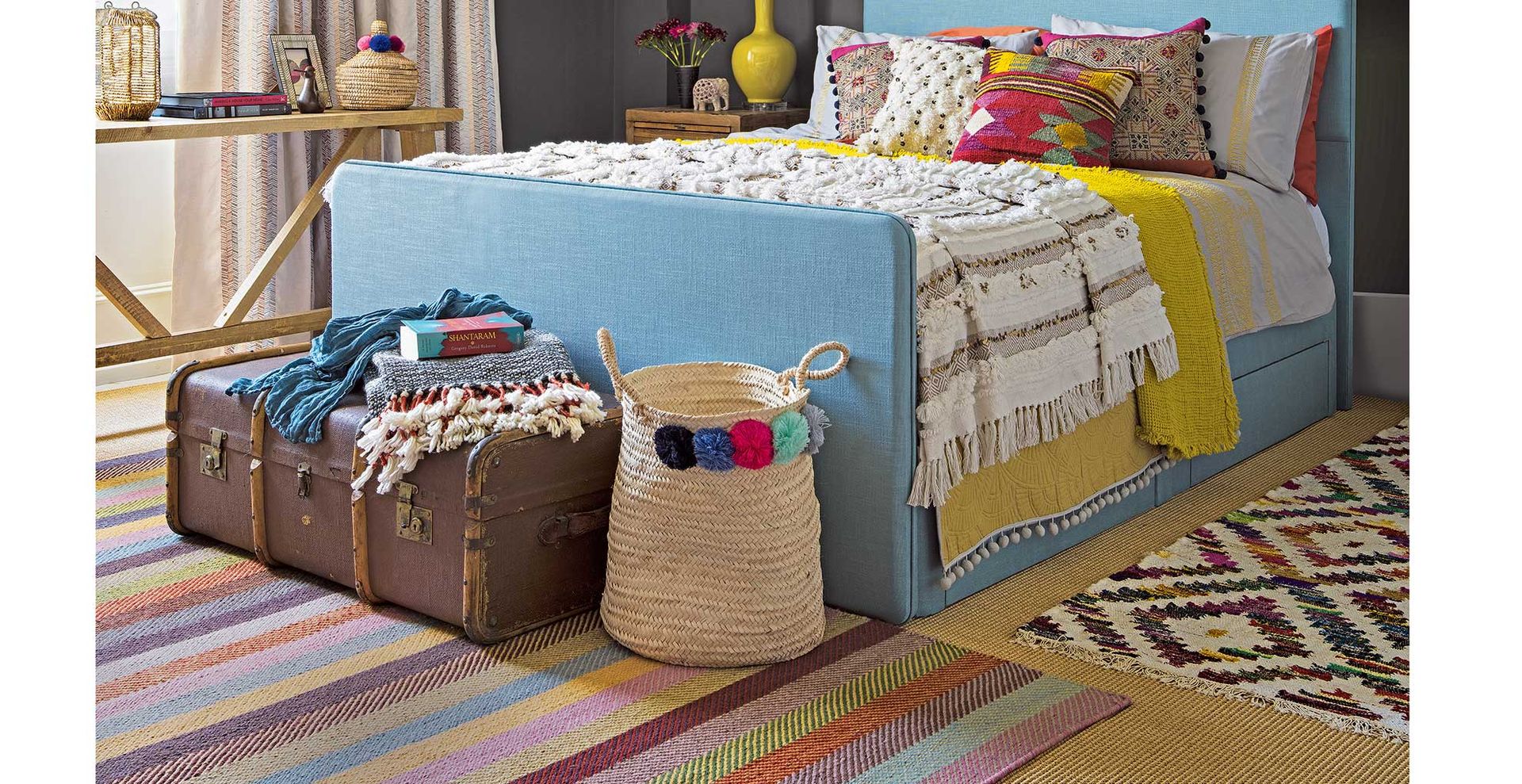 Dark grey bedroom with colouful accessories and rugs surrounding the bed to show how to make a bedroom cosy