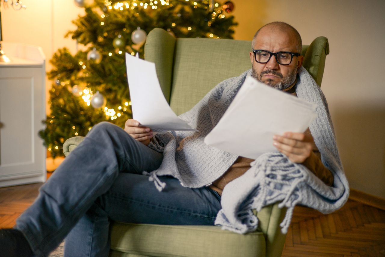 Man sitting in a chair looking at paperwork, Christmas tree in background