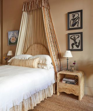 canopy bed in a beige bedroom with a floral bed skirt and burl wood bedside tables