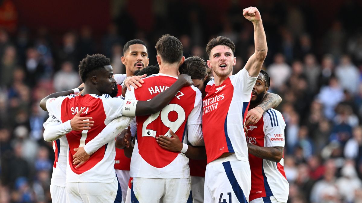 Arsenal players celebrate a goal in a huddle with Declan Rice turned to the camera pumping his fist.