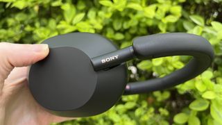 Sony WH-1000XM5 med aktiv støydemping holdes foran en busk
