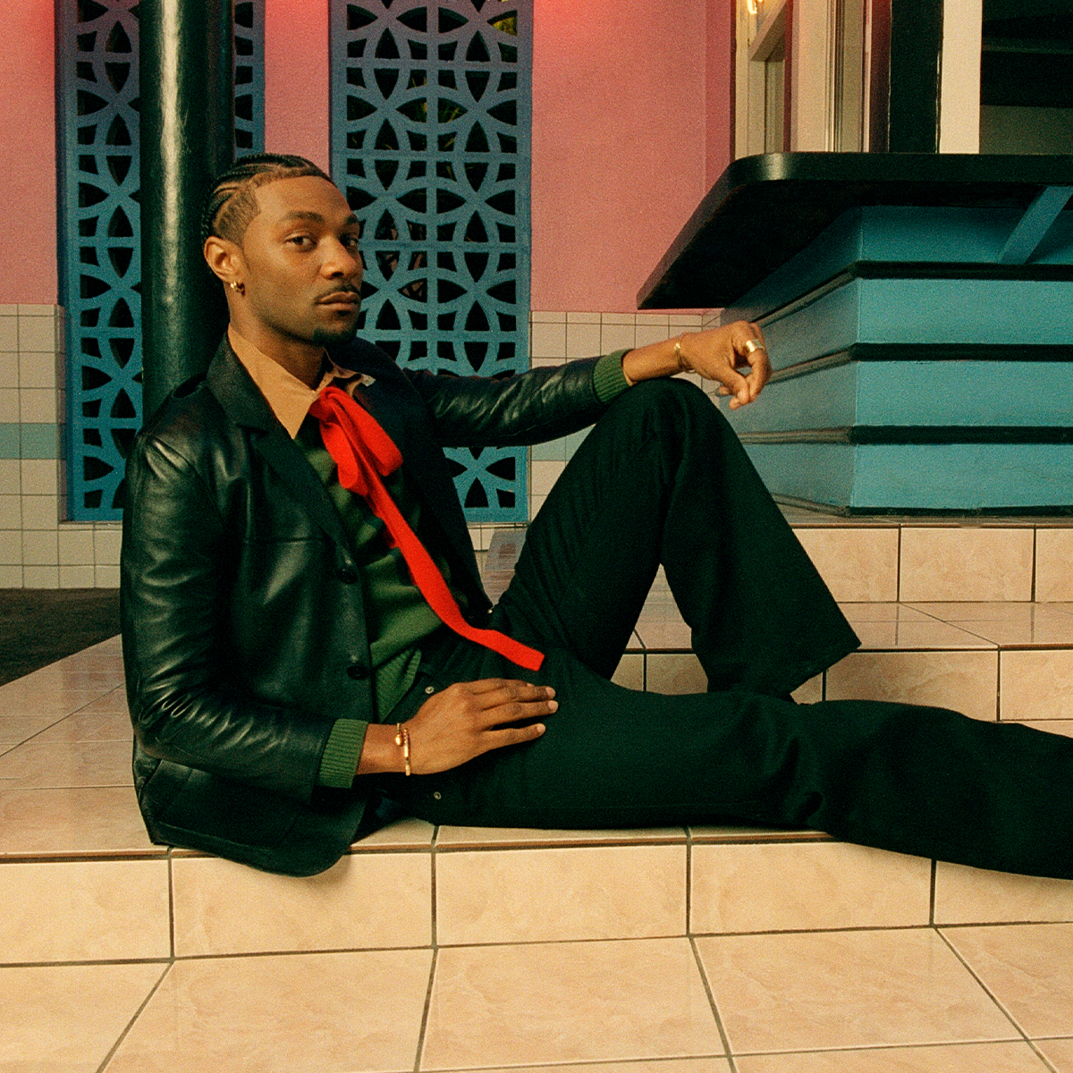 Jonathan Daviss wears a red tie, black leather jacket, and black jeans.