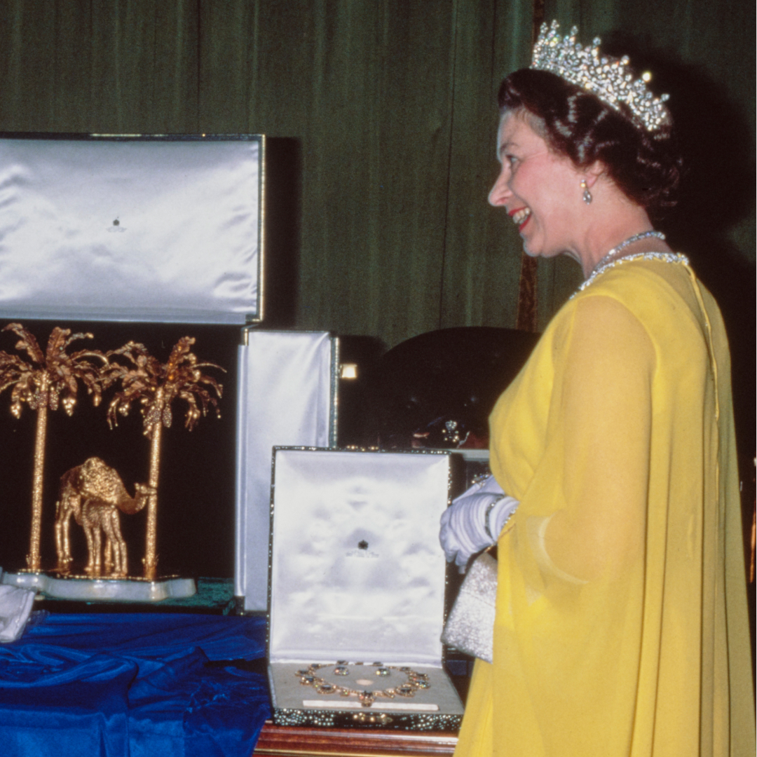 Queen Elizabeth wearing a yellow gown and tiara opening a box of jewelry
