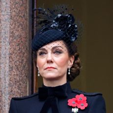 Kate Middleton wearing a black coat with poppy brooches and a black hat with a veil looking serious