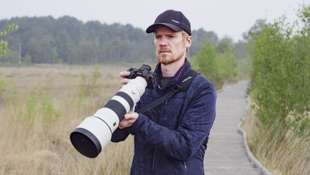Man holding the Sony FE 400-800mm F6.3-8 G OSS supertelephoto zoom lens, he's standing on a boardwalk in a nature reserve