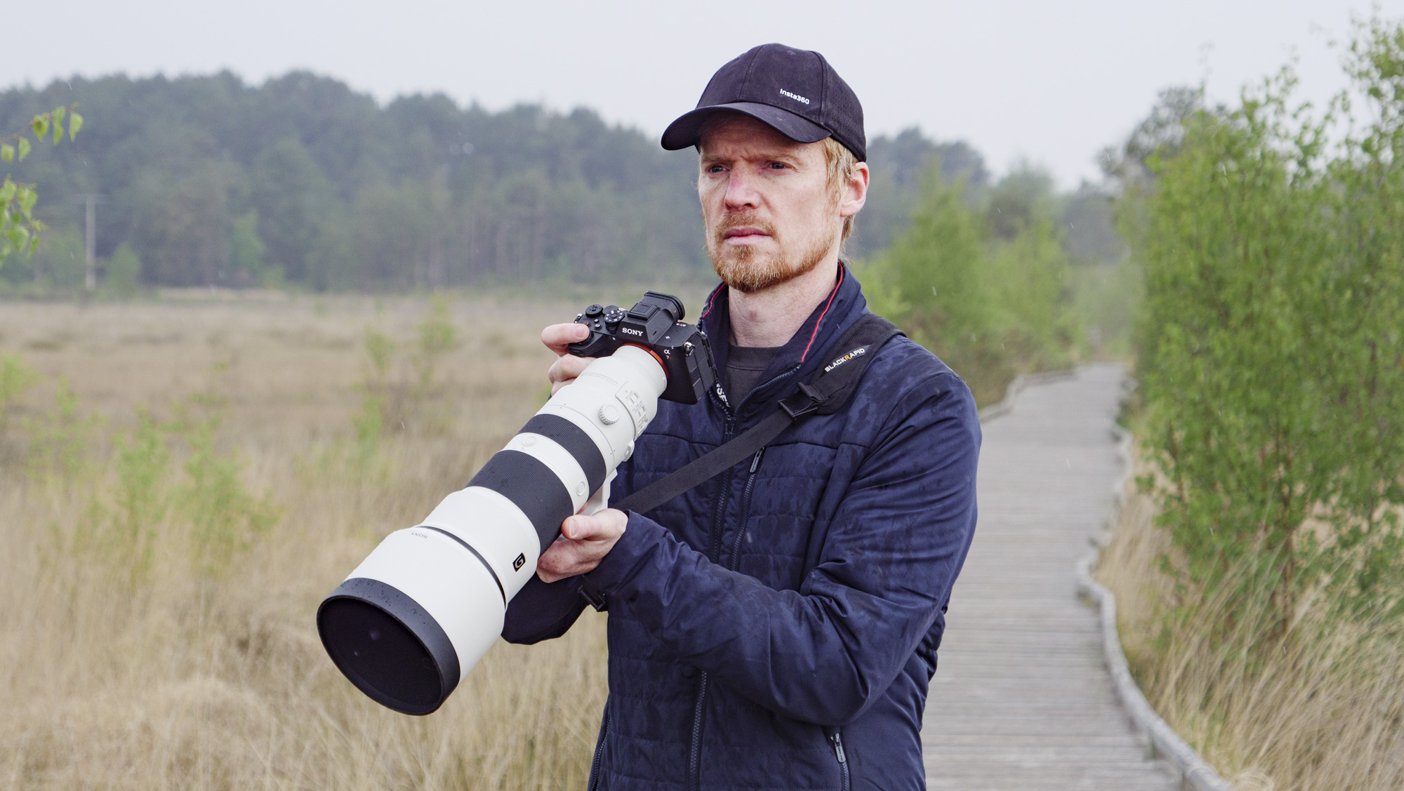 Man holding the Sony FE 400-800mm F6.3-8 G OSS supertelephoto zoom lens, he's standing on a boardwalk in a nature reserve