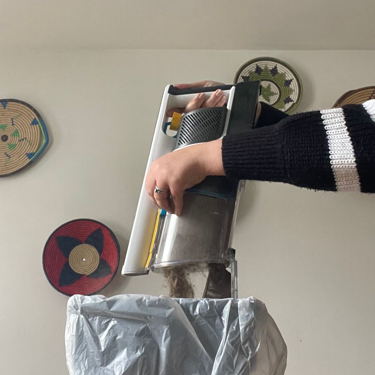 Emptying the Shark PowerPro into a bin in front of a white wall with colourful baskets on it