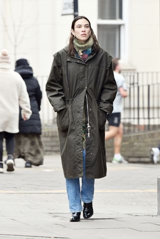 Alexa Chung wears jeans, patent leather boots, a long green jacket and scarf.