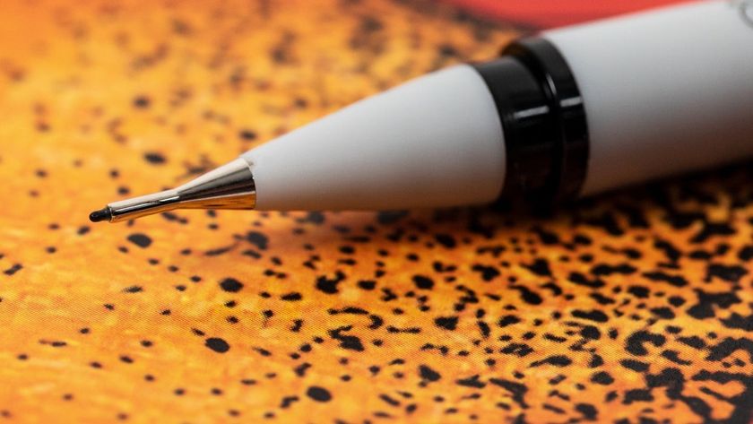 A close-up, shallow depth-of-field shot of the tip of a light gray mechanical pencil, a Winsor &amp; Newton fineliner, with black accents, resting on a textured orange and black patterned surface.