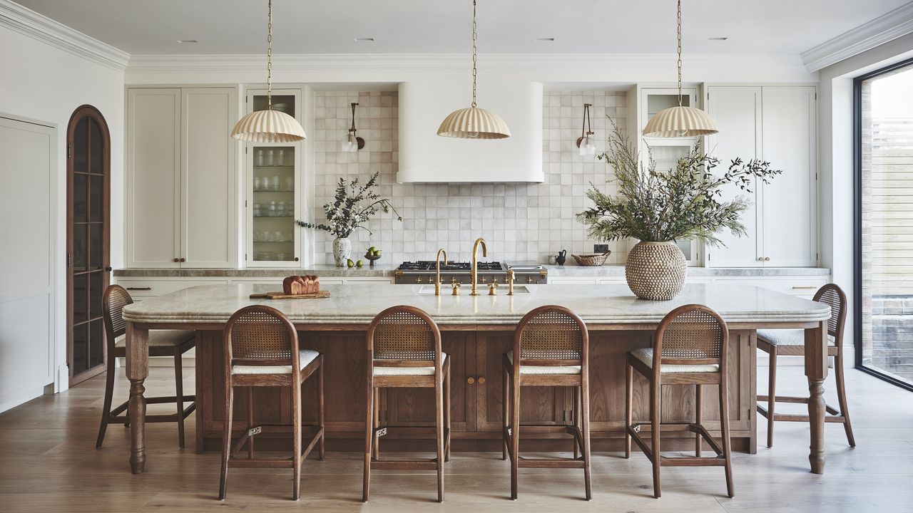 A kitchen with a large wooden island with a marble top and ogee edge that acts like a dining table with stools around it